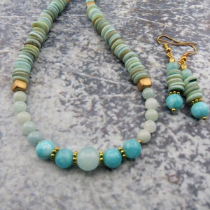 May include: A turquoise and gold necklace and earrings set. The necklace is made with round turquoise beads and gold spacers. The earrings are made with turquoise beads and gold spacers.