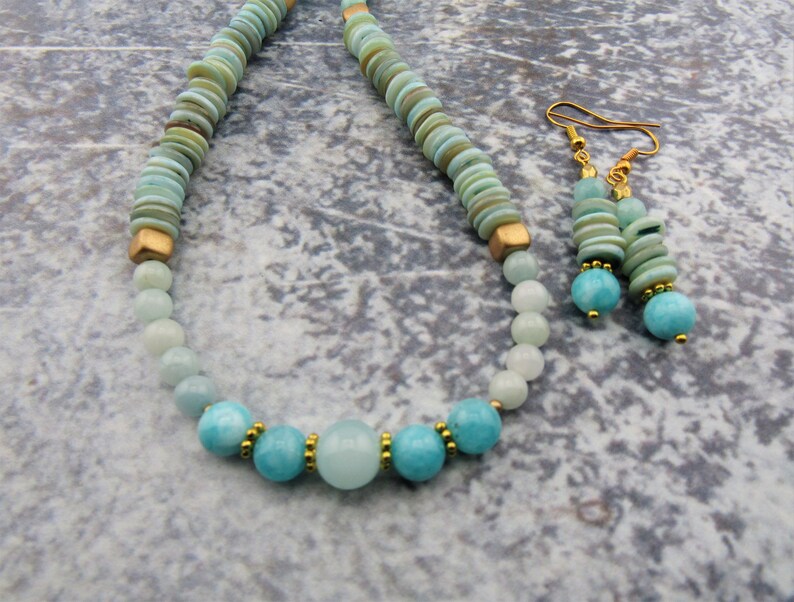 May include: A turquoise and gold necklace and earrings set. The necklace is made with round turquoise beads and gold spacers. The earrings are made with turquoise beads and gold spacers.