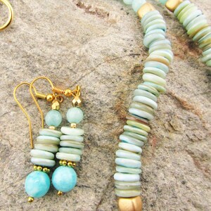 May include: A turquoise and gold necklace and earrings set. The necklace is made with turquoise beads and gold spacers. The earrings are made with turquoise beads and gold hooks.