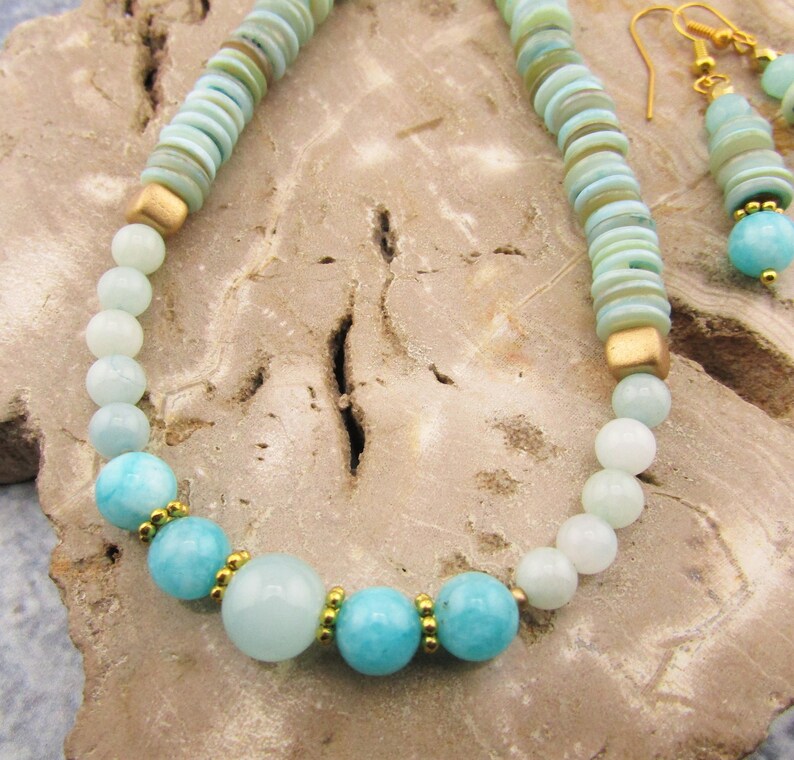 May include: A turquoise and gold necklace and earrings set. The necklace features round turquoise beads and gold spacers. The earrings are drop earrings with turquoise beads and gold accents.