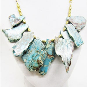 May include: A gold chain necklace with a statement piece of blue and white jasper stone. The stone is cut into irregular shapes and is a statement piece.