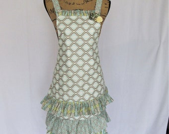 Peut inclure: Un tablier à motif turquoise et marron avec un bas à volants. Le tablier a un imprimé floral sur le volant du bas et une petite fleur en embellissement sur le haut.