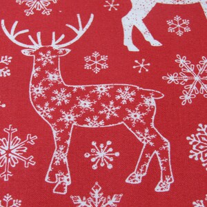 May include: Red fabric with a repeating pattern of white reindeer and snowflakes. The reindeer are outlined in white and filled with snowflake designs. The snowflakes vary in size and shape.