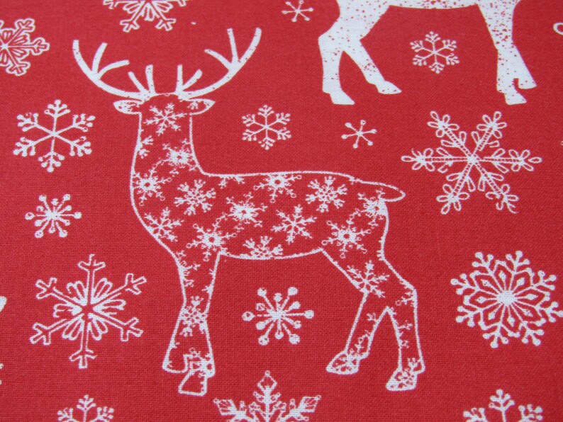 May include: Red fabric with a repeating pattern of white reindeer and snowflakes. The reindeer are outlined in white and filled with snowflake designs. The snowflakes vary in size and shape.
