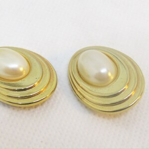 May include: A pair of gold tone clip-on earrings with a faux pearl center.