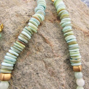 May include: A double-strand necklace made of light blue and green beads with gold accents. The beads are round and flat, and they are strung on a thin gold chain.