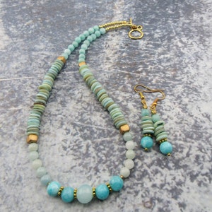 May include: A light blue and green gemstone necklace and earrings set with gold accents. The necklace features a variety of round and flat beads, while the earrings are simple and dangle.