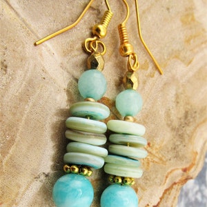 May include: Gold dangle earrings with aqua blue and white layered beads. The earrings feature a round aqua blue bead at the bottom.