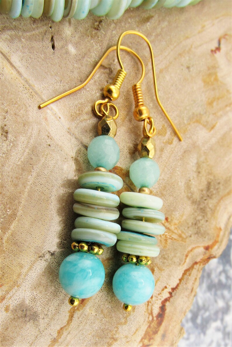 May include: Gold dangle earrings with aqua blue and white layered beads. The earrings feature a round aqua blue bead at the bottom.