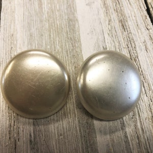 May include: A pair of round, off-white, pearl-like earrings. The earrings are smooth and have a slight sheen.
