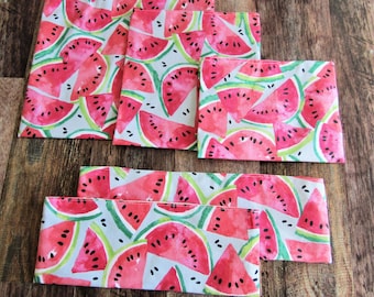 May include: Set of six white cotton napkins with a watercolor print of pink and green watermelons. The napkins are folded and stacked on a wooden surface.