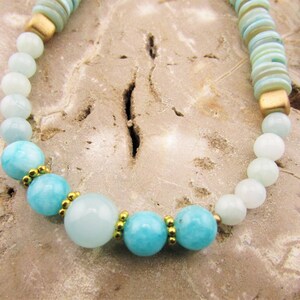 May include: A light blue and white beaded necklace with gold accents. The necklace features round beads of varying sizes and a mix of light blue and white colors. The gold accents are small and evenly spaced throughout the necklace.