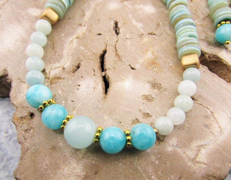 May include: A light blue and white beaded necklace with gold accents. The necklace features round beads of varying sizes and a mix of light blue and white colors. The gold accents are small and evenly spaced throughout the necklace.