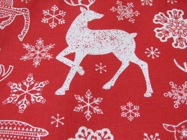 May include: Red fabric with a repeating pattern of white reindeer and snowflakes. The reindeer are stylized with antlers and the snowflakes vary in design. The overall theme is festive and seasonal, suitable for holiday decorations.