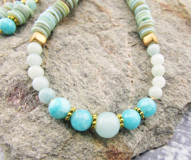 May include: A light blue and white beaded necklace with gold accents. The necklace features round beads and a larger, round, light blue bead in the center.