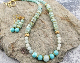 May include: A light blue and green gemstone necklace and matching earrings with gold accents. The necklace features a graduated design with larger, rounder stones at the bottom and smaller, flat stones at the top. The earrings are simple and feature a single, round stone.
