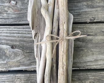 Peut inclure: Un lot de cinq morceaux de bois flotté liés ensemble avec de la ficelle. Le bois flotté est de différentes nuances de brun et de gris, et a un aspect naturel et vieilli.