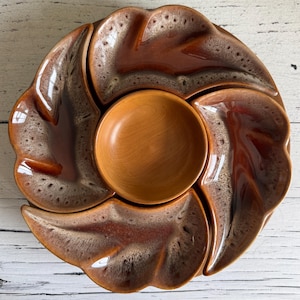 May include: A brown and white ceramic serving dish with four leaf-shaped sections and a central round bowl. The dish is ideal for serving snacks or appetizers.