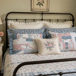 May include: A bed with a dark metal frame, adorned with floral patterned bedding and pillows. The pillows feature patchwork designs in shades of blue, red, and white. A small, square pillow with a floral embroidery is also present. A bedside lamp and a framed floral print complete the scene.