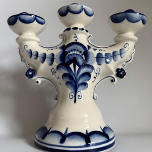 Peut inclure: Un candélabre en céramique blanche à trois bougeoirs, orné de motifs floraux bleus complexes. La base et les supports présentent des bords festonnés, créant un design décoratif et élégant. Un objet de décoration classique.