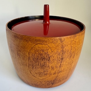May include: A wooden bowl with a red lid and a black rim. The bowl has a natural wood finish and the lid has a glossy red finish.
