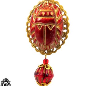 May include: A gold chain necklace with a red scarab beetle pendant and a red faceted bead. The scarab beetle is detailed with gold accents.