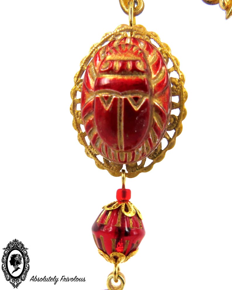 May include: A gold chain necklace with a red scarab beetle pendant and a red faceted bead. The scarab beetle is detailed with gold accents.