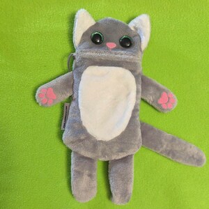 Puede incluir: Una bolsa de felpa gris con forma de gato con detalles blancos en el pecho, las orejas y la barriga. Tiene ojos grandes y brillantes, una nariz rosa y almohadillas en las patas. La bolsa tiene una cremallera y el texto "millasprouts.com".
