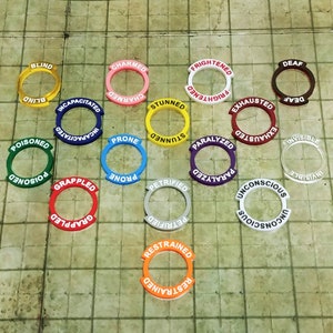 May include: A set of 13 colorful plastic tokens with different status conditions written on them, such as "Blind", "Charmed", "Frightened", "Deaf", "Stunned", "Incapacitated", "Prone", "Paralyzed", "Exhausted", "Invisible", "Petrified", "Grappled", "Unconscious", and "Restrained".