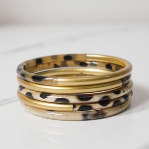 Op de afbeelding: Stapel van vier armbanden. Twee zijn goudkleurig en twee hebben een schildpadpatroon. De armbanden liggen op een wit oppervlak. De tekst "TONKIN HANDICRAFT" staat bovenaan.