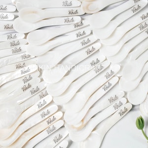 May include: A collection of white mother of pearl spoons with the word "Vinile" engraved on each one. The spoons are arranged in a heart shape.