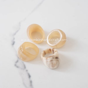 Puede incluir: Cuatro anillos hechos de cuerno natural, con una variedad de patrones y colores. Los anillos son de diferentes tamaños y formas, y todos están hechos de cuerno liso y pulido. Los anillos están sobre una superficie de mármol blanco.