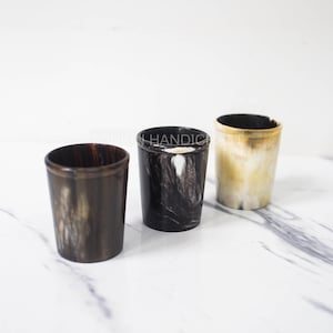 May include: Three horn cups in different colours and patterns. The cups are made of natural horn and have a unique, rustic look.