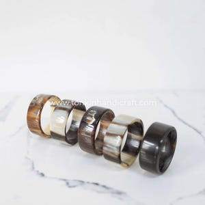 May include: Six handcrafted napkin rings in varying shades of brown and cream. The rings are made of a natural material, with a polished finish. The website tonkinhandicraft.com is visible on the image.