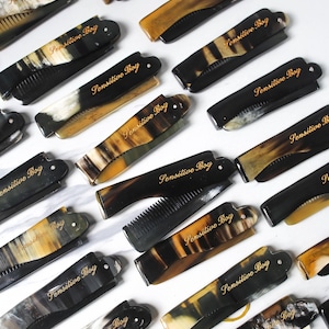 Könnte beinhalten: Eine Sammlung von schwarzen und braunen Klappkämmen mit goldener Aufschrift "Sensitive Boy".