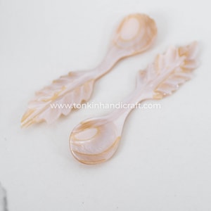 Puede incluir: Dos cucharas pequeñas hechas de nácar con un diseño de hoja en el mango. Las cucharas son de color rosa pálido con remolinos marrones.