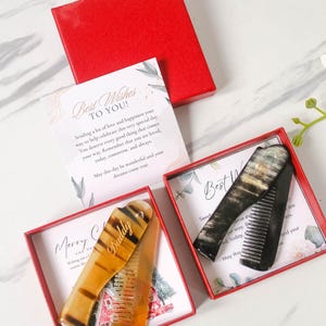 May include: Two red gift boxes each containing a comb. The comb in the left box is brown and has the word "Daddy" engraved on it. The comb in the right box is black. The boxes contain a card with the text "Best Wishes To You!" and "Merry Christmas and a Happy New Year".