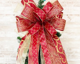 May include: A red and gold Christmas tree topper bow with a large, decorative bow and long, flowing tails. The bow is made of satin ribbon with a gold floral pattern.