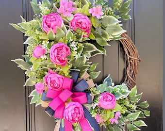 Può includere: Una ghirlanda floreale rosa e verde con un grande fiocco rosa. La ghirlanda è realizzata con fiori e verde artificiali ed è perfetta per una decorazione per porta primaverile o estiva.