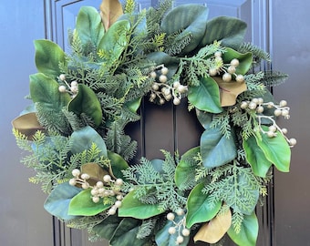 Può includere: Una ghirlanda di foglie di magnolia verde e marrone con bacche dorate. La ghirlanda è appesa a una porta nera.