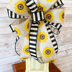 Puede incluir: Un gran lazo de girasol con cinta rayada en blanco y negro. El lazo est&aacute; atado alrededor de una linterna blanca.