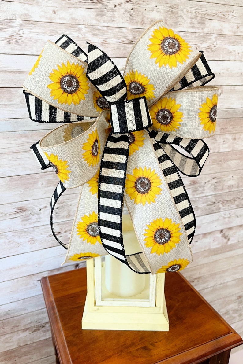 Puede incluir: Un gran lazo de girasol con cinta rayada en blanco y negro. El lazo est&aacute; atado alrededor de una linterna blanca.