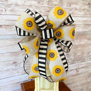 Puede incluir: Un gran lazo a rayas blanco y negro con estampado de girasol. El lazo est&aacute; hecho de arpillera y tiene un estilo r&uacute;stico y de granja.