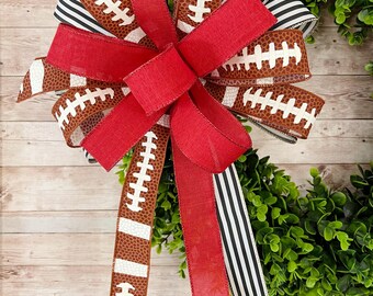 May include: A red, white, and brown football-themed wreath bow with a black and white striped ribbon.