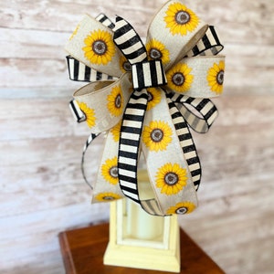 Puede incluir: Un gran lazo de rayas blancas y negras con girasoles, perfecto para a&ntilde;adir un toque de encanto r&uacute;stico a la decoraci&oacute;n de tu hogar.