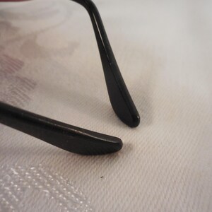May include: Close-up of black eyeglasses. The image focuses on the temple arms and the frame, showcasing the sleek design and the smooth, glossy finish. The arms are curved and end in a rounded tip.