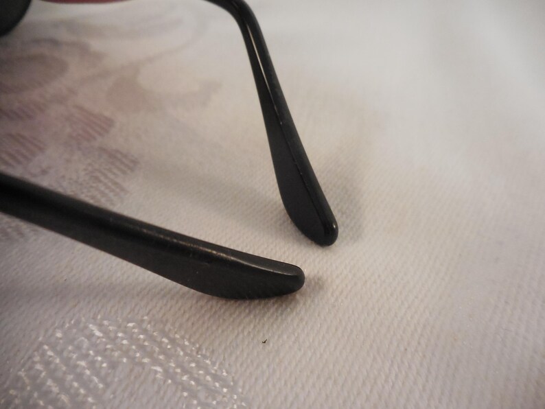 May include: Close-up of black eyeglasses. The image focuses on the temple arms and the frame, showcasing the sleek design and the smooth, glossy finish. The arms are curved and end in a rounded tip.