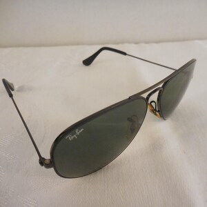 May include: Aviator-style sunglasses with dark frames and green lenses. The Ray-Ban logo is visible on the lens. The sunglasses have a classic design, suitable for various styles.