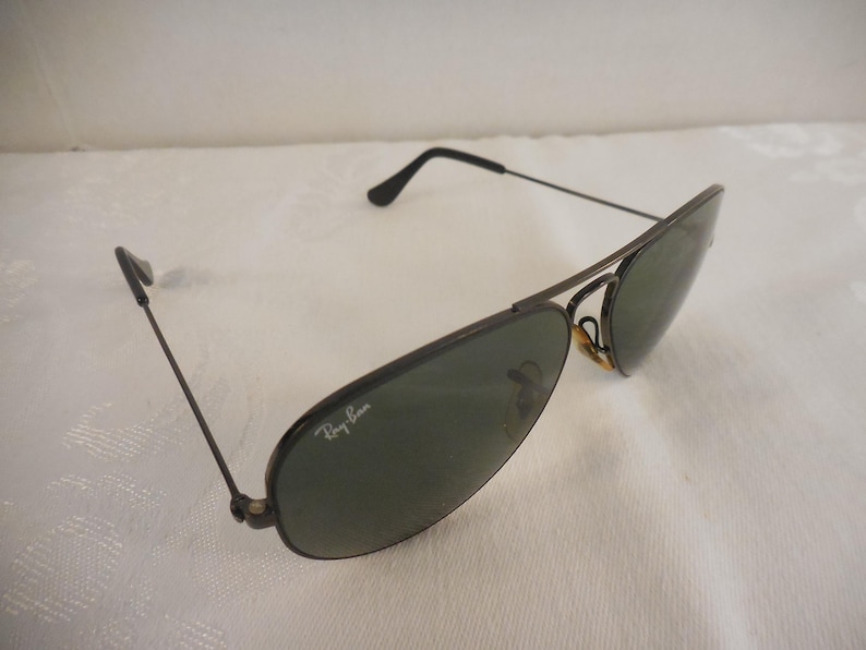 May include: Aviator-style sunglasses with dark frames and green lenses. The Ray-Ban logo is visible on the lens. The sunglasses have a classic design, suitable for various styles.