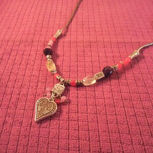 May include: A necklace with a silver heart pendant and a beaded chain. The heart pendant has an ornate design and the words "Listen to your heart". The beads are various colors, including pink, red, and clear.